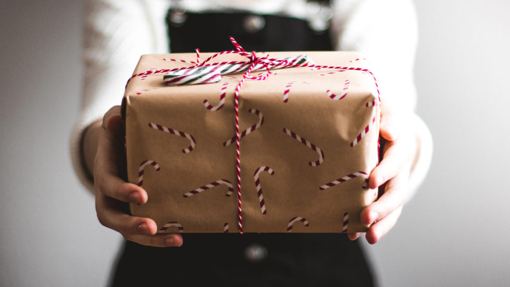 Person holds out a gift wrapped with reused and recycled materials