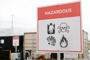 Household hazardous waste warning sign at a collection site, showing corrosive, toxic, explosive and flammable hazard symbols.